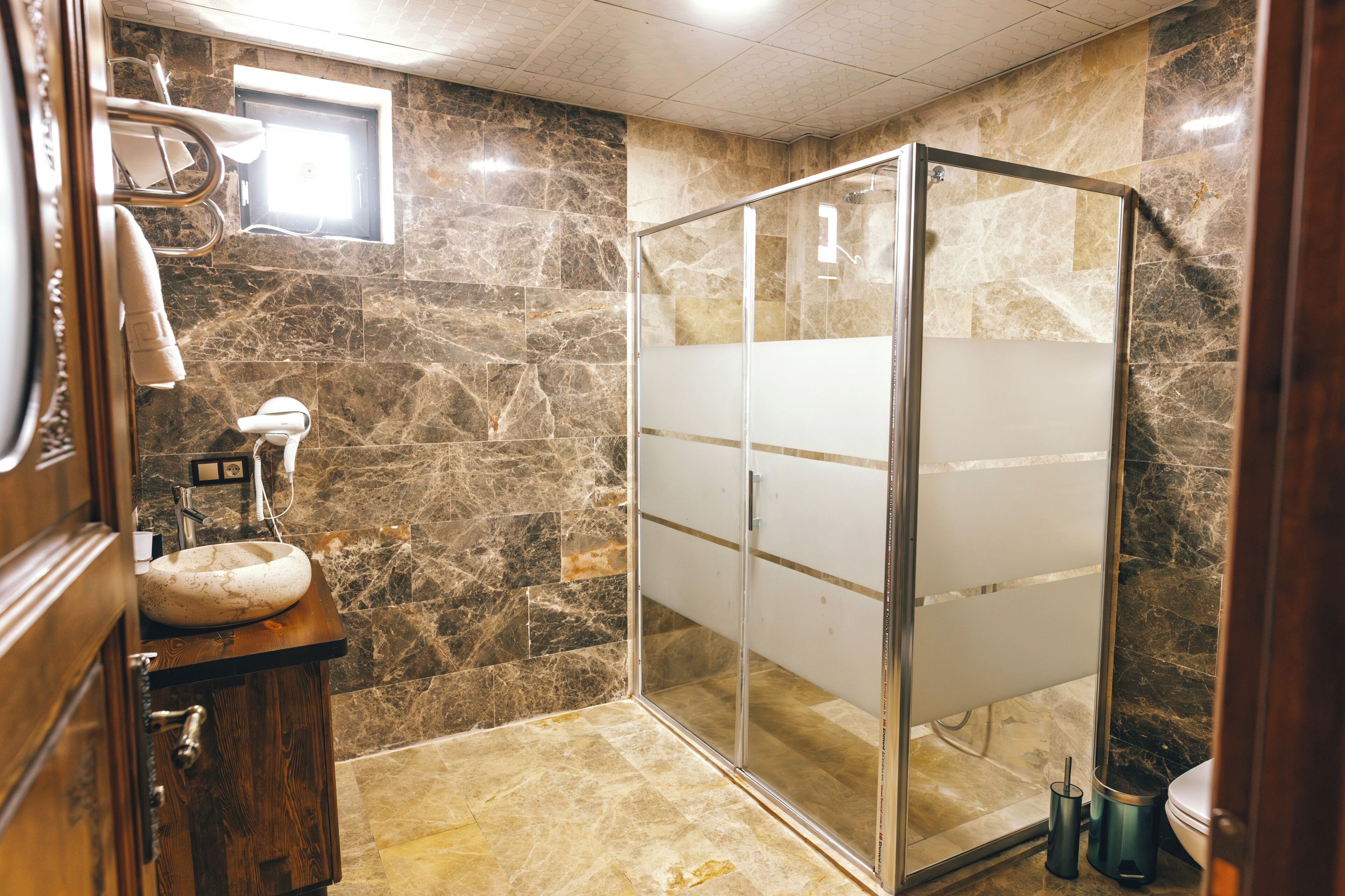 A bathroom with a marble wall, a wooden vanity, a glass shower enclosure, and a toilet.