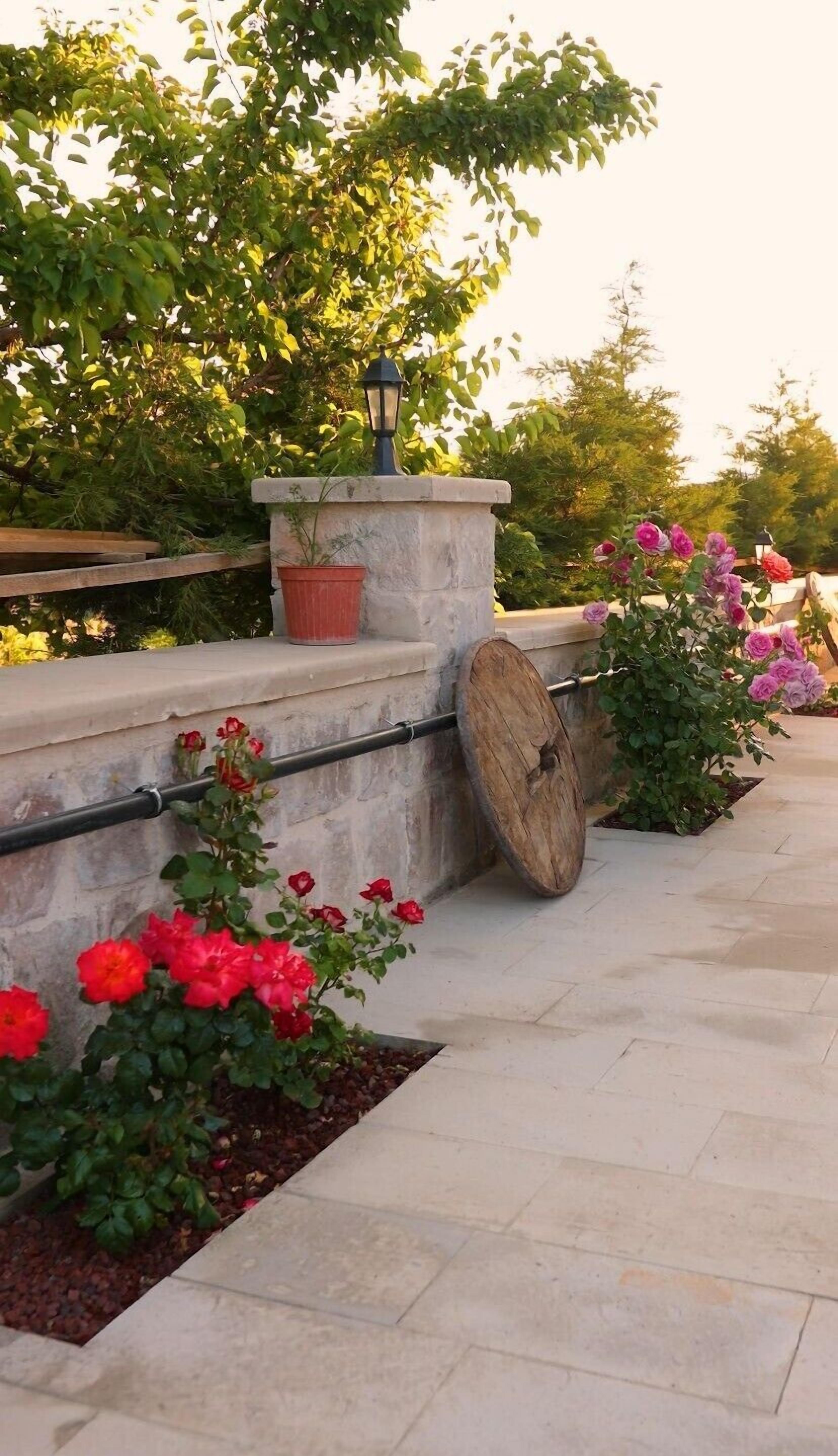 A stone bench with a metal railing, surrounded by potted plants and flowers.