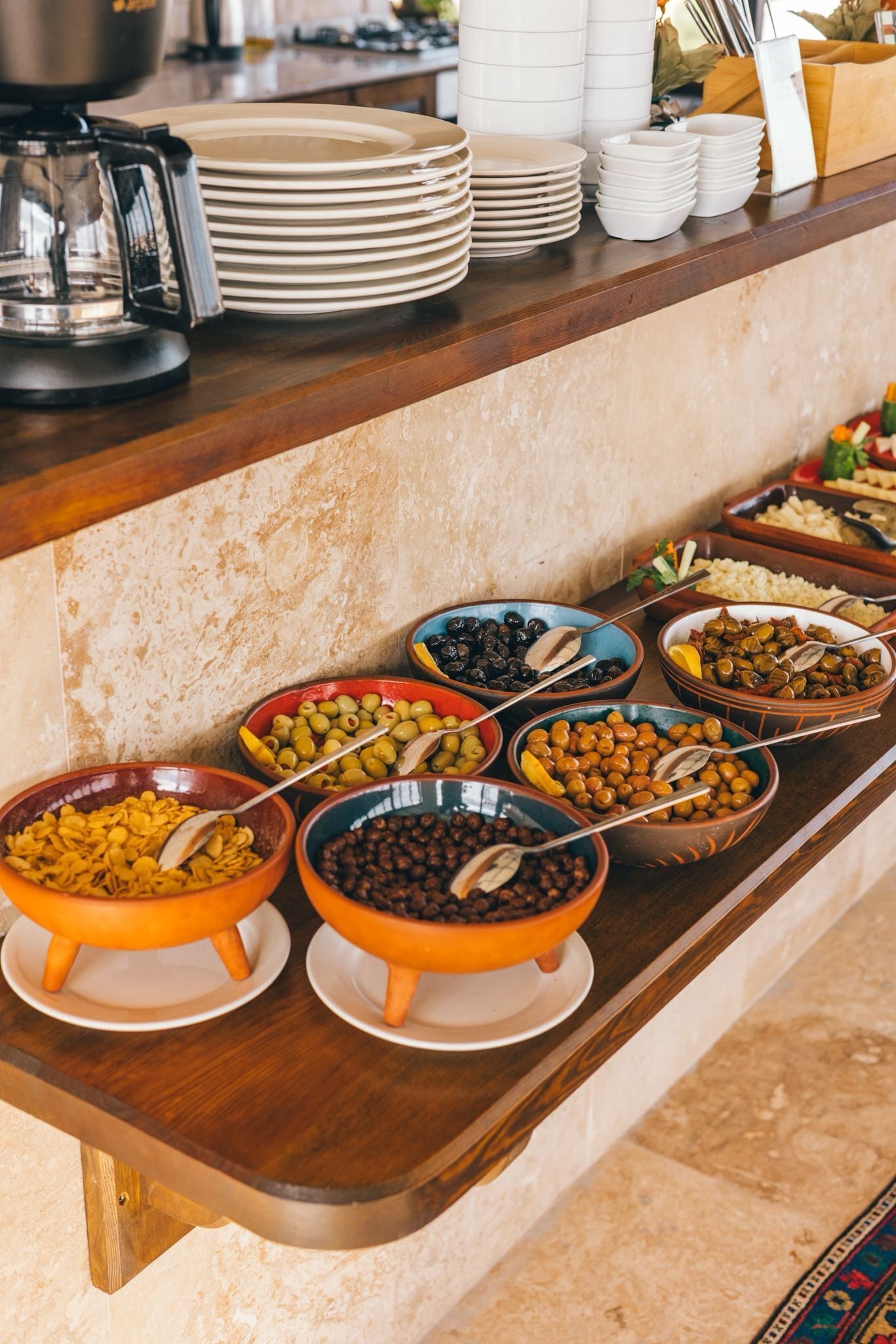 Montaje de bufé con diferentes alimentos en fuentes y platos sobre una barra de madera.