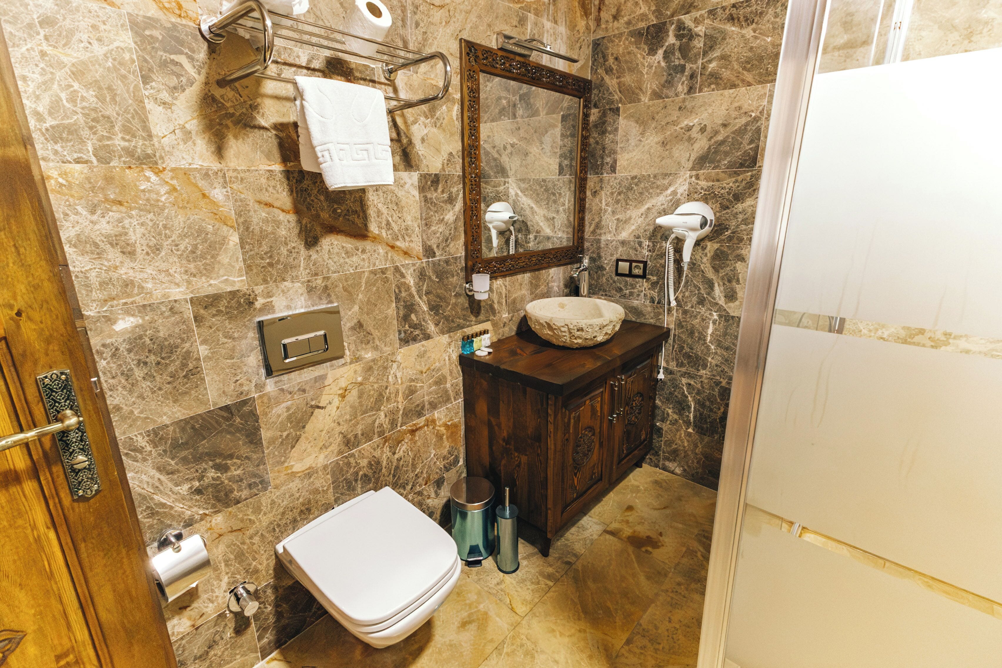 Een badkamer met een marmeren vloer, een houten wastafelmeubel met een wastafel, een toilet en een spiegel.
