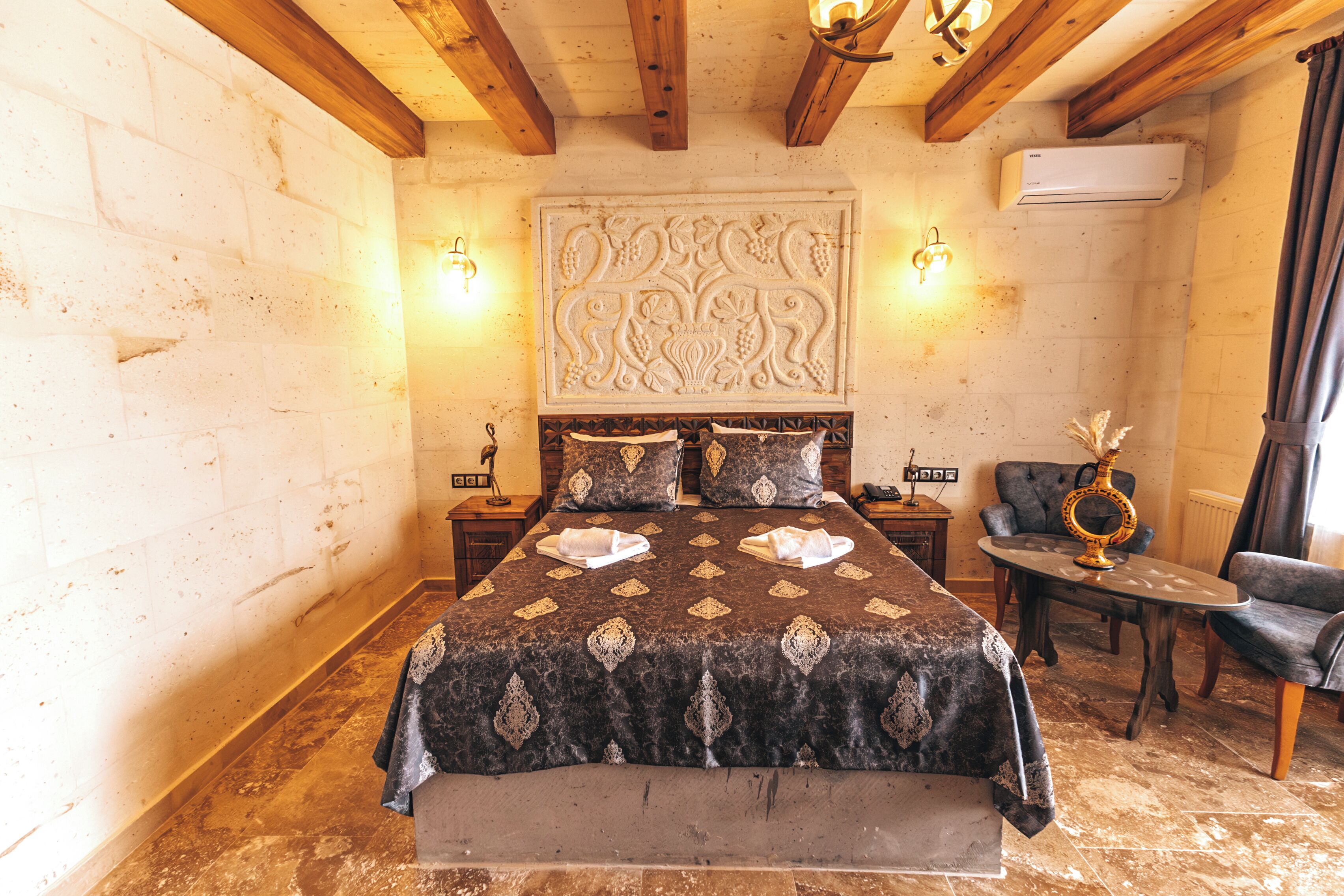 A bedroom with a large bed, two bedside tables, a chair, and a decorative wall panel.