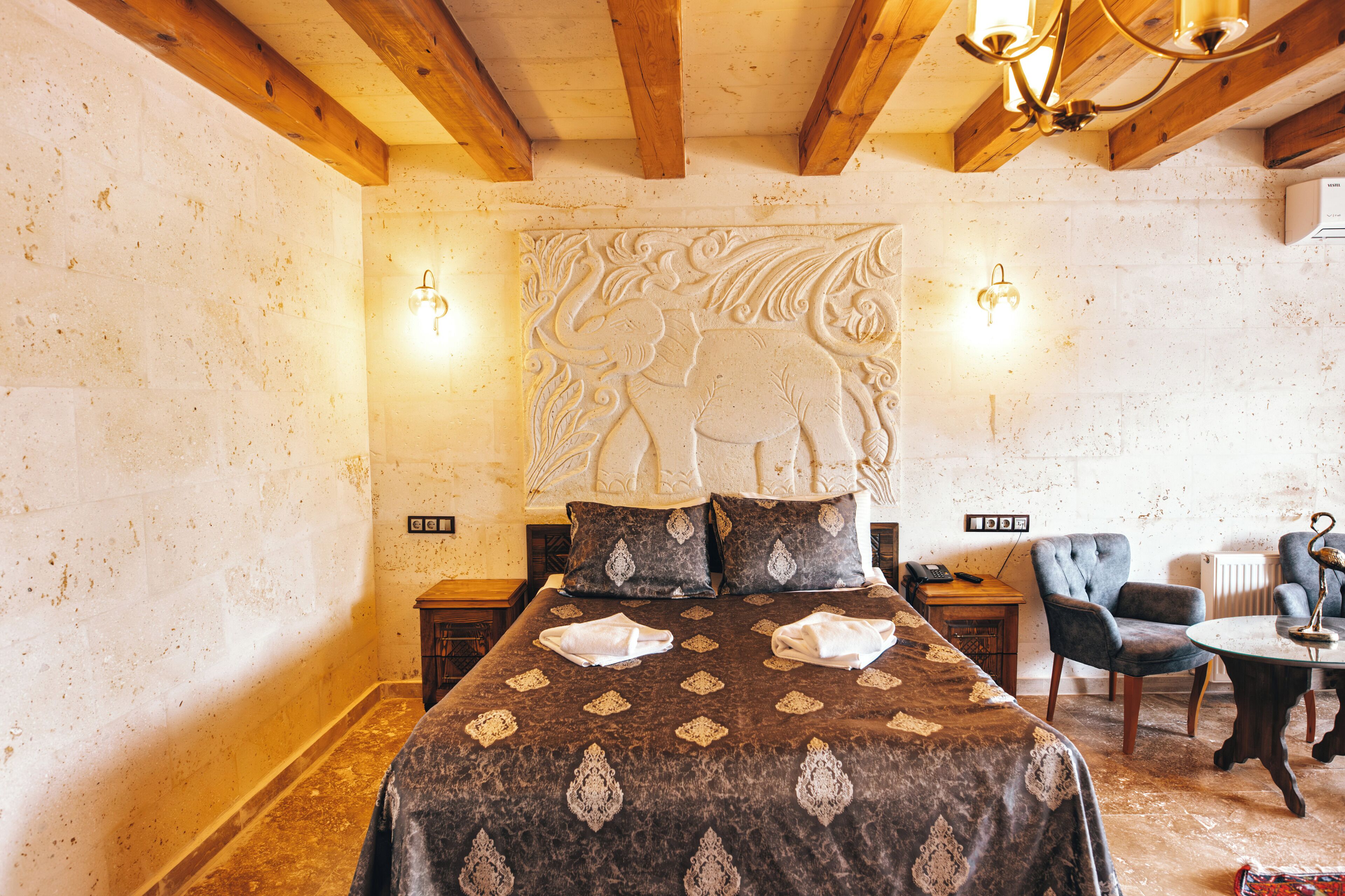 A room with a bed, a chair, a table, and a wall with a decorative carving.