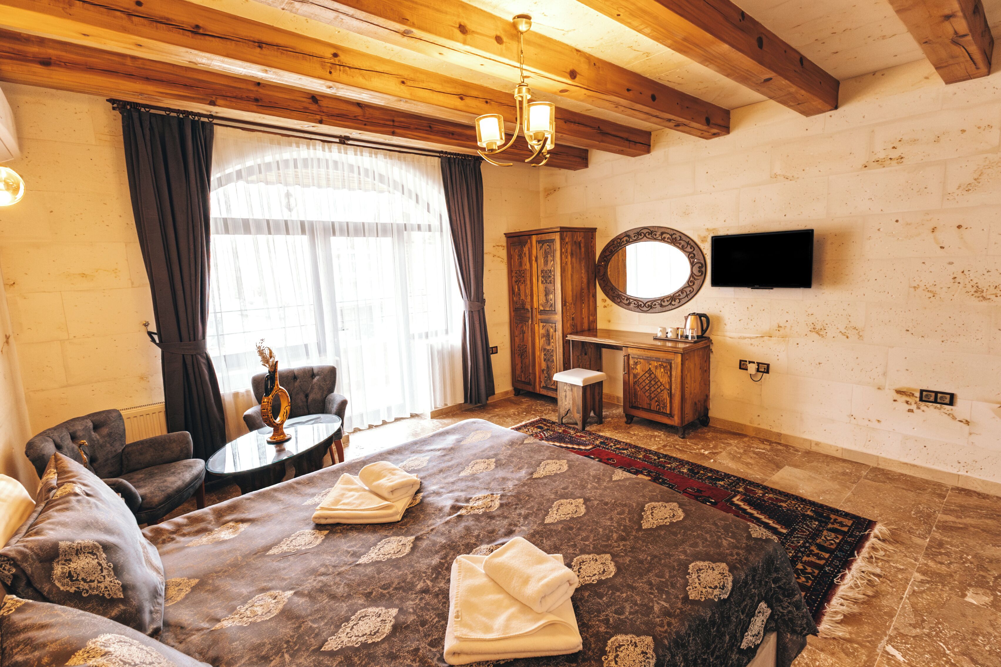 A hotel room with a large bed, a small table, a sofa, a mirror, and a TV.