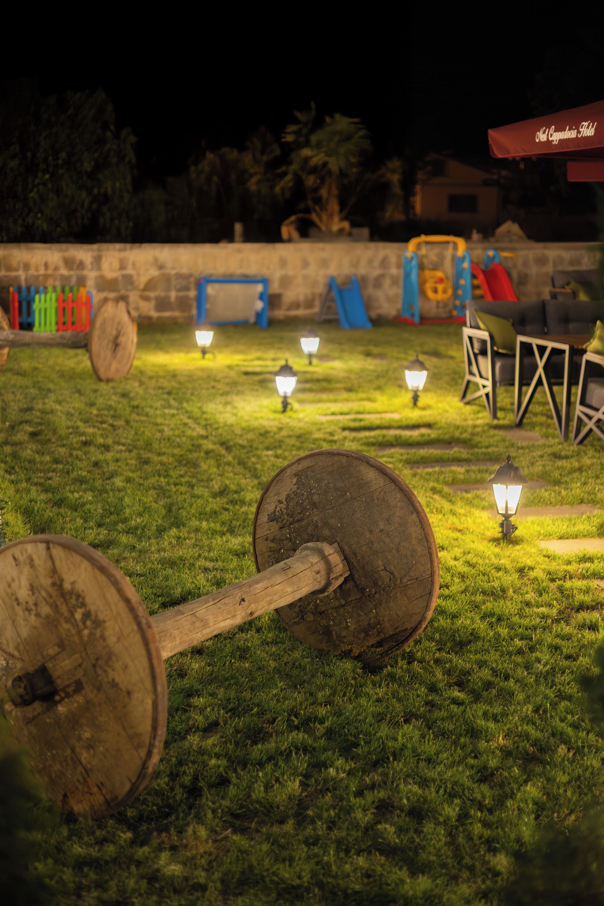 Un espacio al aire libre con césped, una banca de madera, una mesa y una estructura de juegos al fondo.