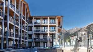 Un hôtel à plusieurs étages, doté de balcons, d’une cour dallée et surplombant un paysage montagneux.