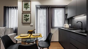 Egy praktikus, kisebb méretű konyha, étkezősarokkal, melyben üveglapos asztal, fekete székek és egy modern tűzhely található.