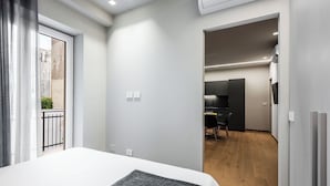 Egy modern szállodai szoba, amelyben egy nagy ágy, egy kis íróasztal található, és kilátás nyílik a külső erkélyre.