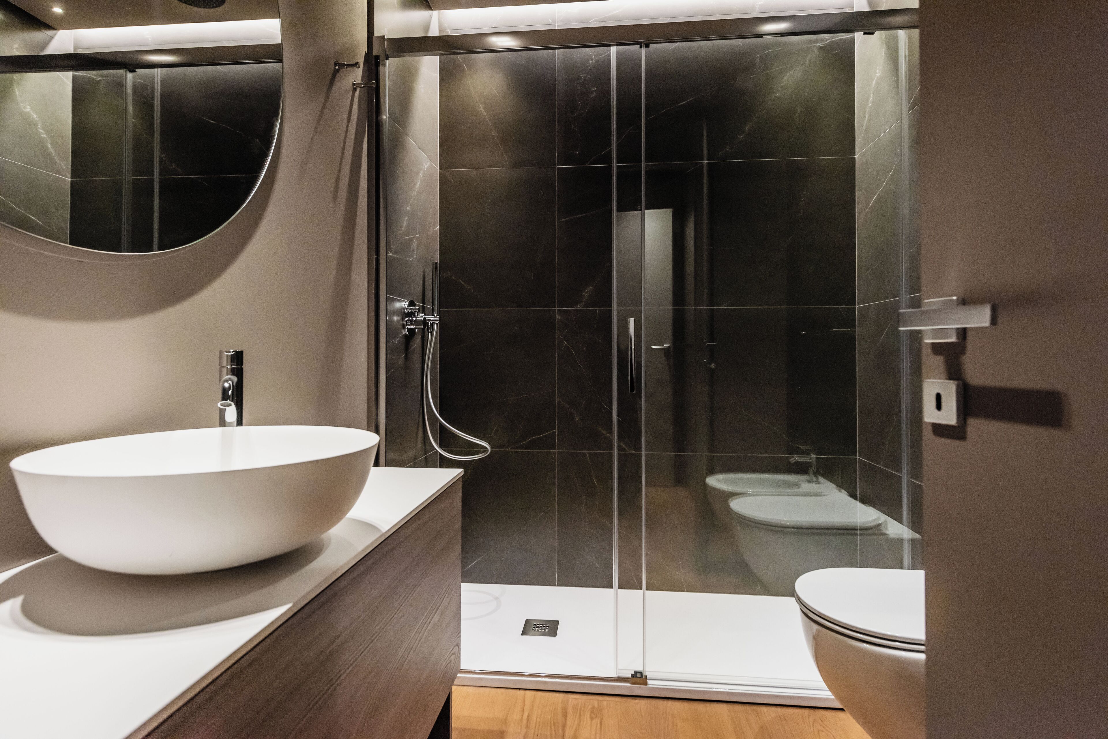 Un bany modern amb un gran lavabo blanc de disseny, dutxa amb envàs de vidre i vàter.
