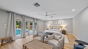 A spacious bedroom with a large bed, a ceiling fan, and a view of a swimming pool through glass doors.