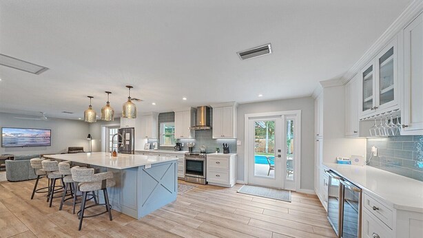 A modern kitchen with a large island, bar stools, a dining area, and a view of an outdoor pool.