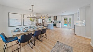 A modern kitchen with a central island, wooden flooring, and a dining area with blue chairs.