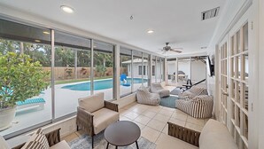 A spacious patio with large windows, a ceiling fan, and a view of a swimming pool.