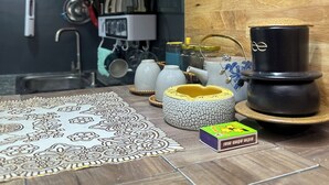 Una cuina amb un fesó estampat, un rentamans i diferents utensilis de cuina, incloent una tetera i tasses.