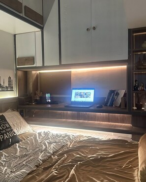 Une chambre à coucher comprenant un lit, un bureau avec un ordinateur portable, une étagère remplie de livres et un meuble fixé au mur.