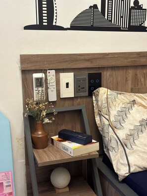 Une pièce bien rangée, avec un lit, une table de chevet ornée d’un vase contenant des fleurs séchées, un livre et une télécommande.