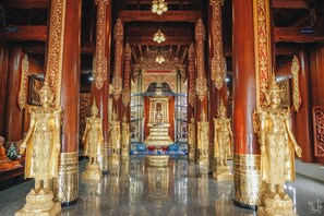 L’intérieur d’un temple, orné de statues et de piliers dorés, avec un autel central et un sol réfléchissant.