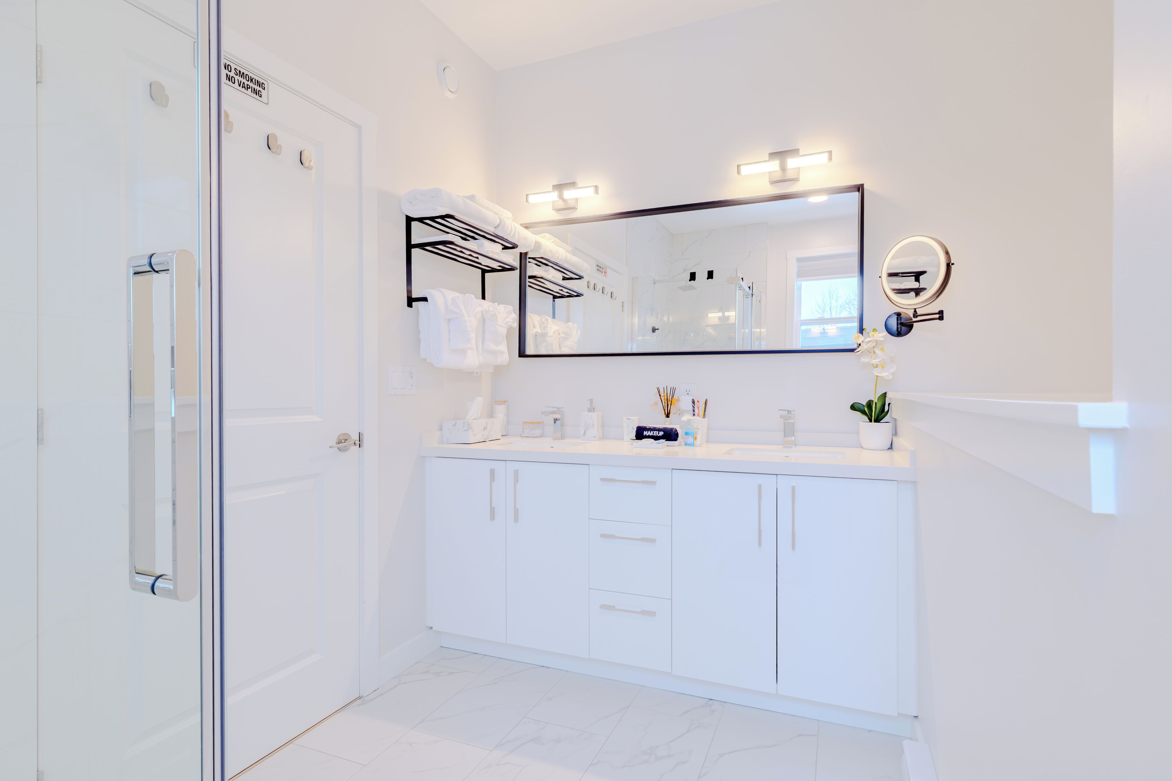 A modern bathroom with a white vanity, a large mirror, and a 'NO SMOKING' sign.