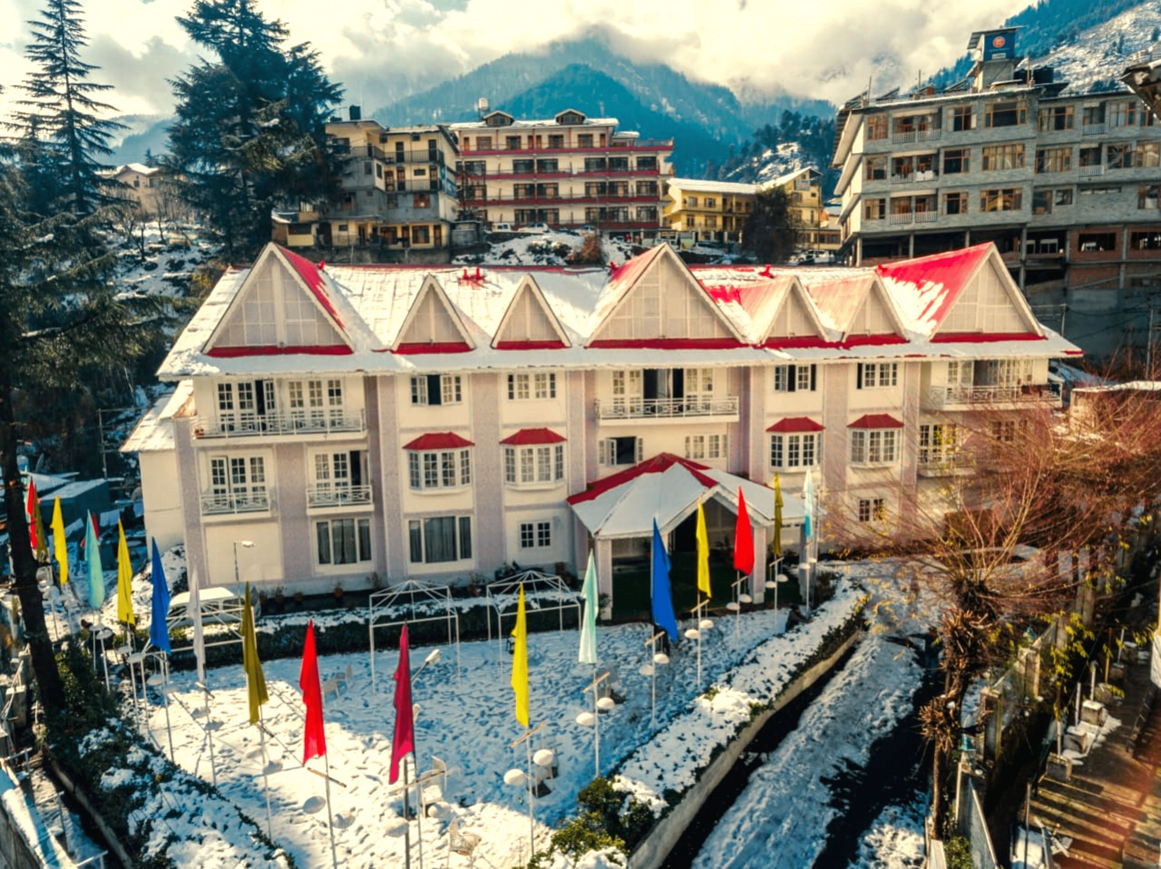 A hotel with multiple floors, a central courtyard with colorful flags, and a mountainous backdrop.