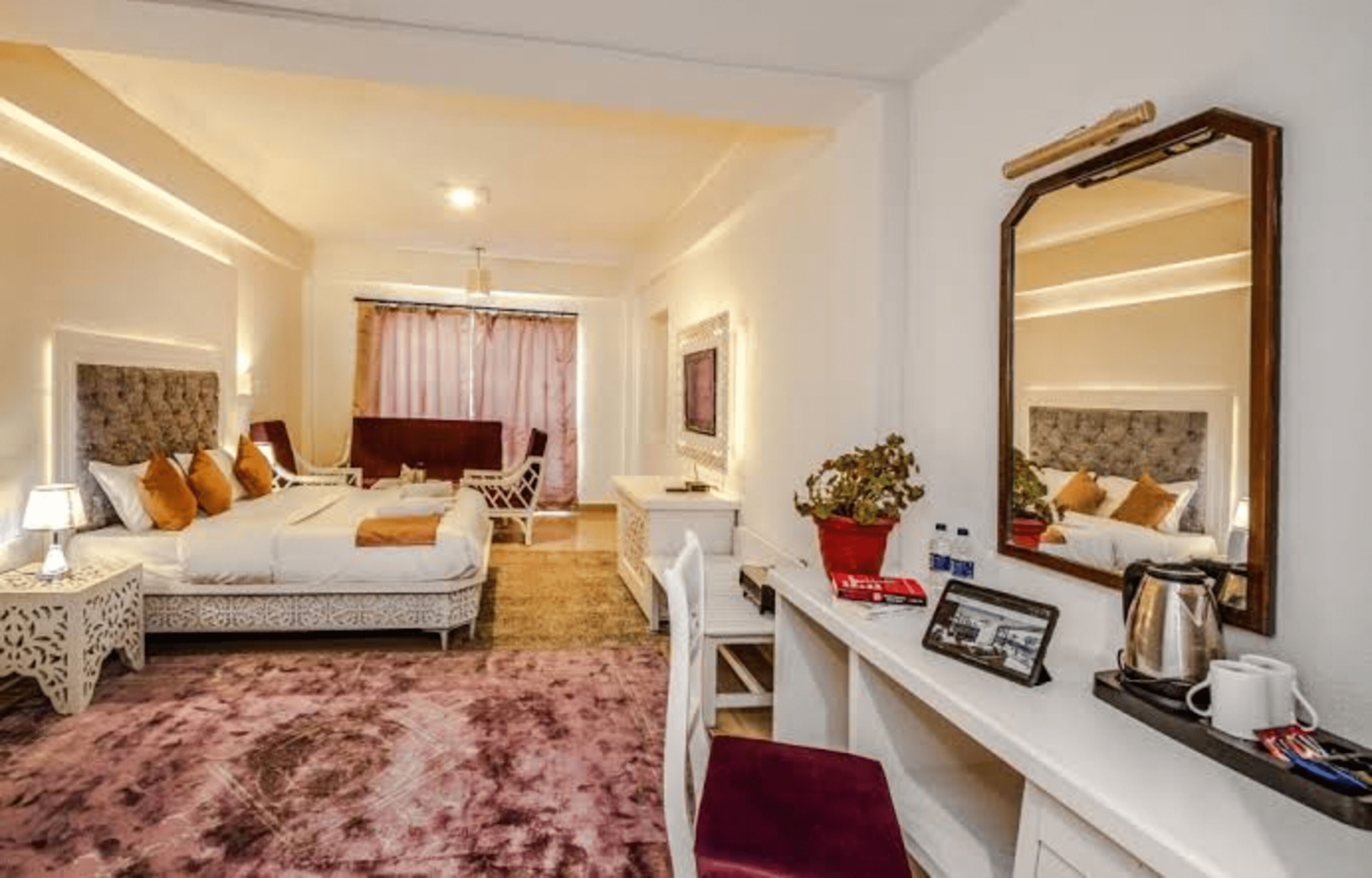 A hotel room with a bed, bedside table, desk, chair, and a large mirror.