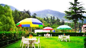 An outdoor seating area with tables and chairs, surrounded by lush greenery and mountains in the background. - Hotel Snow Princess  (Manali)