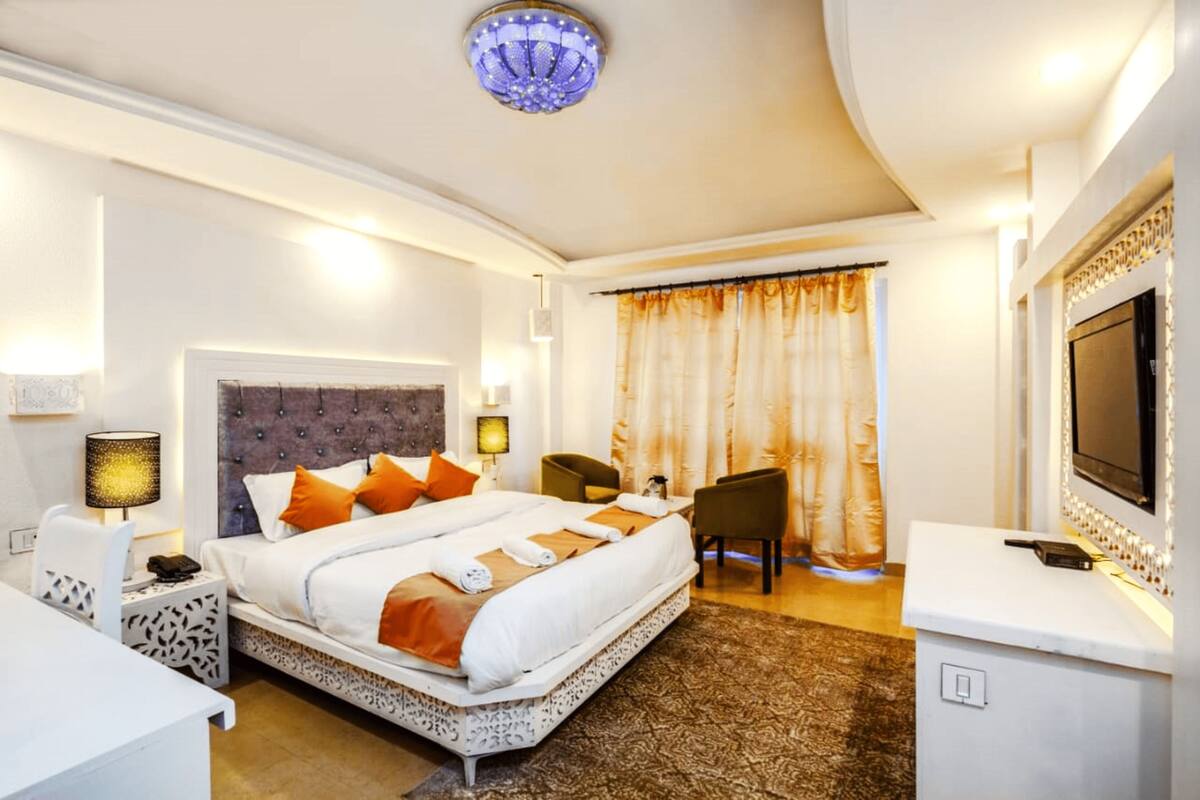 Une chambre d’hôtel avec un grand lit, un bureau, une chaise, une télévision et un lustre.