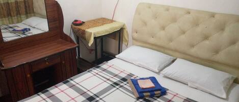 A hotel room with a bed, a bedside table, a mirror, and a wall socket.