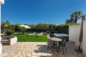 Zona patio con pavimento in pietra, vasca idromassaggio e due poltrone da relax.