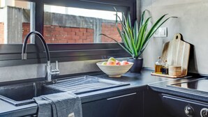 A modern kitchen with a black countertop, a stainless steel sink, a window, and a potted plant. - Sanders Old Port Thessaloniki (Thessaloniki)