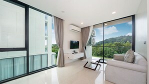 Ein modernes Wohnzimmer mit großem Fenster, Flachbildfernseher, einer Couch und einem kleinen Tisch.