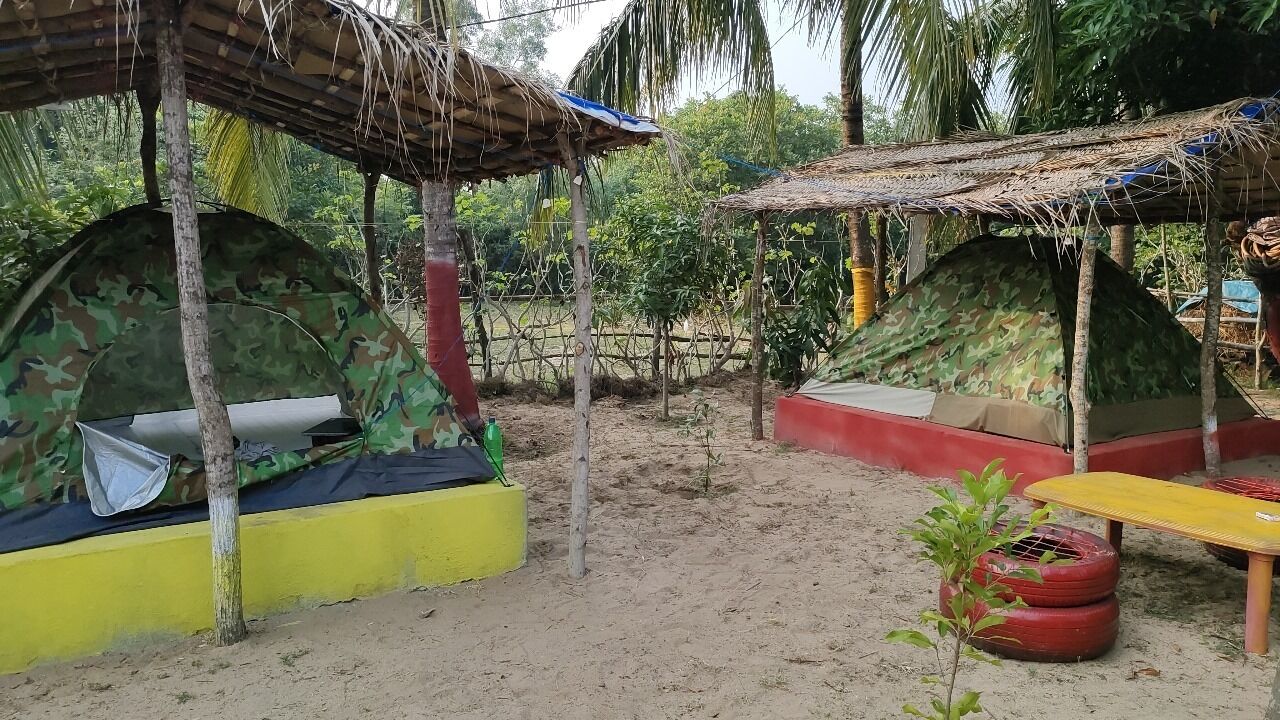 A sandy outdoor area with two camouflaged tents, a yellow bench, and a small table.