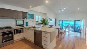 A modern kitchen with built-in appliances, a dining area with a view, and a spacious living area. - Shorelines 17 - Hamilton Island  (Hamilton Island)