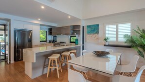 A modern kitchen with a central island, wooden stools, and a dining table with white chairs. - Shorelines 17 - Hamilton Island  (Hamilton Island)