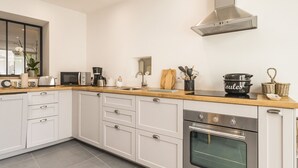 Une cuisine moderne avec des armoires blanches, une hotte de cuisinière en acier inoxydable, un four encastré et un plan de travail en bois.