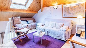 Une chambre mansardée chaleureuse avec un plafond en pente, une grande lucarne, un lit, un canapé, une petite table et une carte accrochée au mur.