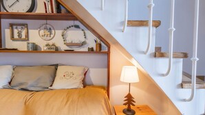 Une chambre à coucher comprenant un lit, une table de chevet, une lampe, une horloge et une étagère avec des livres et des objets de décoration.