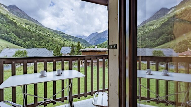 Un balcon avec une table et des chaises, donnant sur un paysage montagneux.