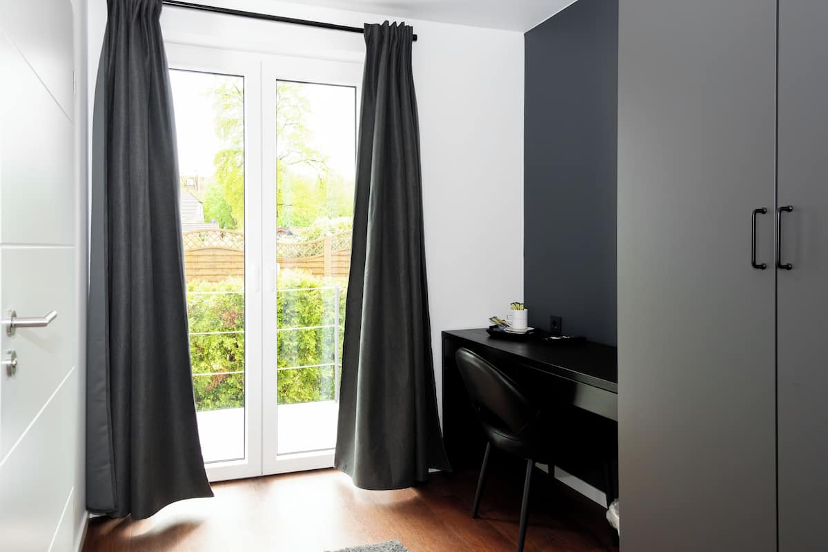 A room with a sliding glass door, a black desk, and a chair.