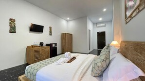 A hotel room with a bed, wooden headboard, a television mounted on the wall, a wardrobe, and a small table with a kettle and cups. - Rai Wood Carver and Homestay (Ubud)