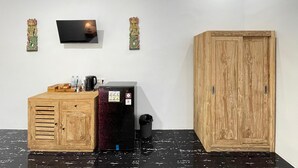 A room with a wooden cabinet, a black refrigerator, a television mounted on the wall, and a wooden wardrobe. - Rai Wood Carver and Homestay (Ubud)