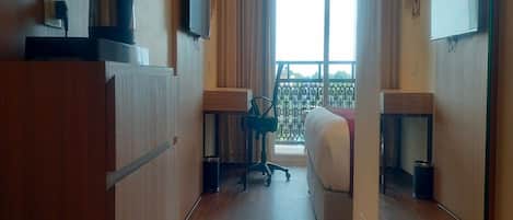 A hotel room with a bed, a desk, a chair, a TV, and a balcony with a railing.