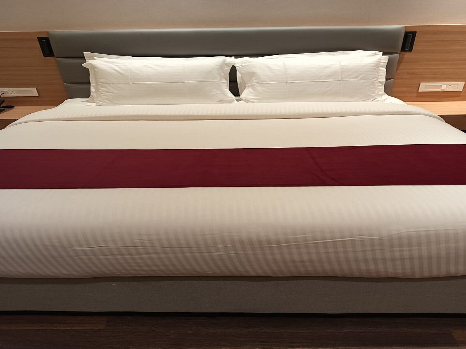 Ein Bett mit grauem Kopfteil, weißen Kissen und roten Akzenten.