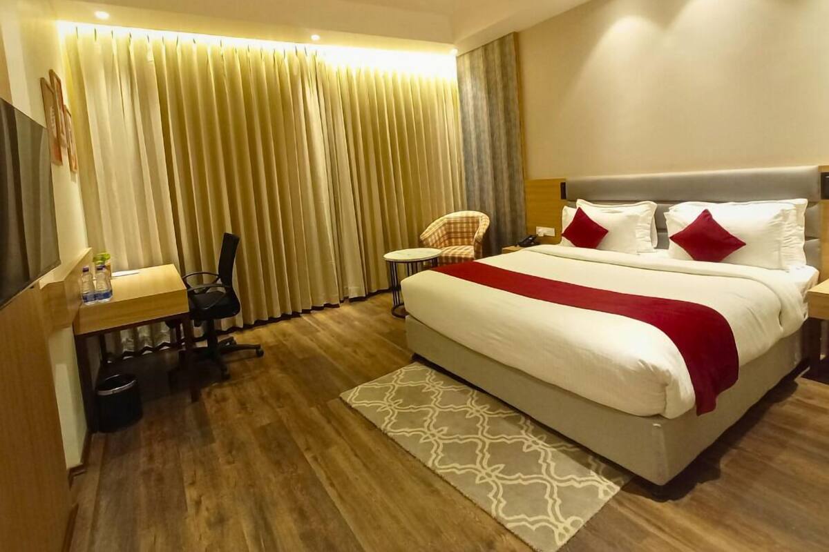 A hotel room with a large bed, a desk with a chair, a small table, and a TV.