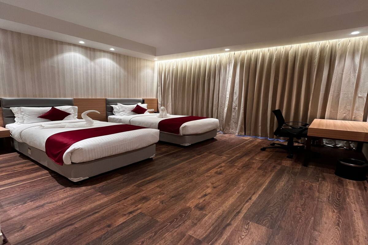 A hotel room with two beds, a wooden floor, and a desk with a chair.