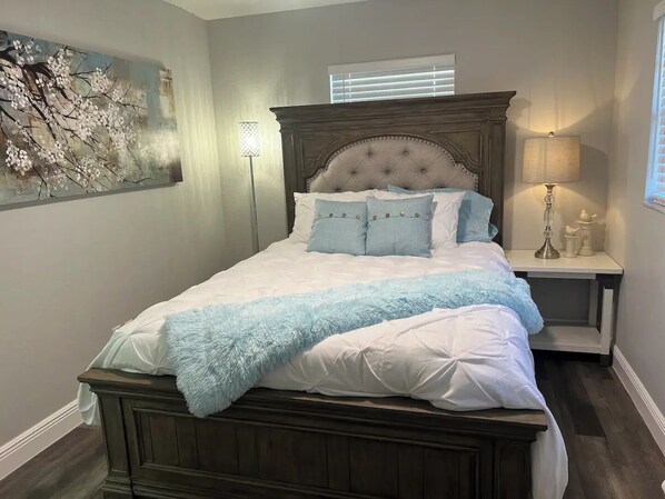 A bedroom with a large bed, a headboard, a bedside table with a lamp, and a wall-mounted artwork. - Sunny Springs Oasis (Ocala)
