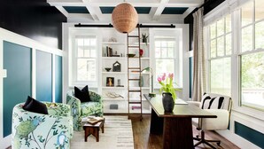 Un salon aux murs de couleur turquoise, doté d’un plancher en bois, d’une bibliothèque, d’une échelle et d’une table sur laquelle est posé un vase rempli de fleurs.