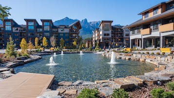 Un resort con varias construcciones, un estanque central con fuentes y montañas al fondo.