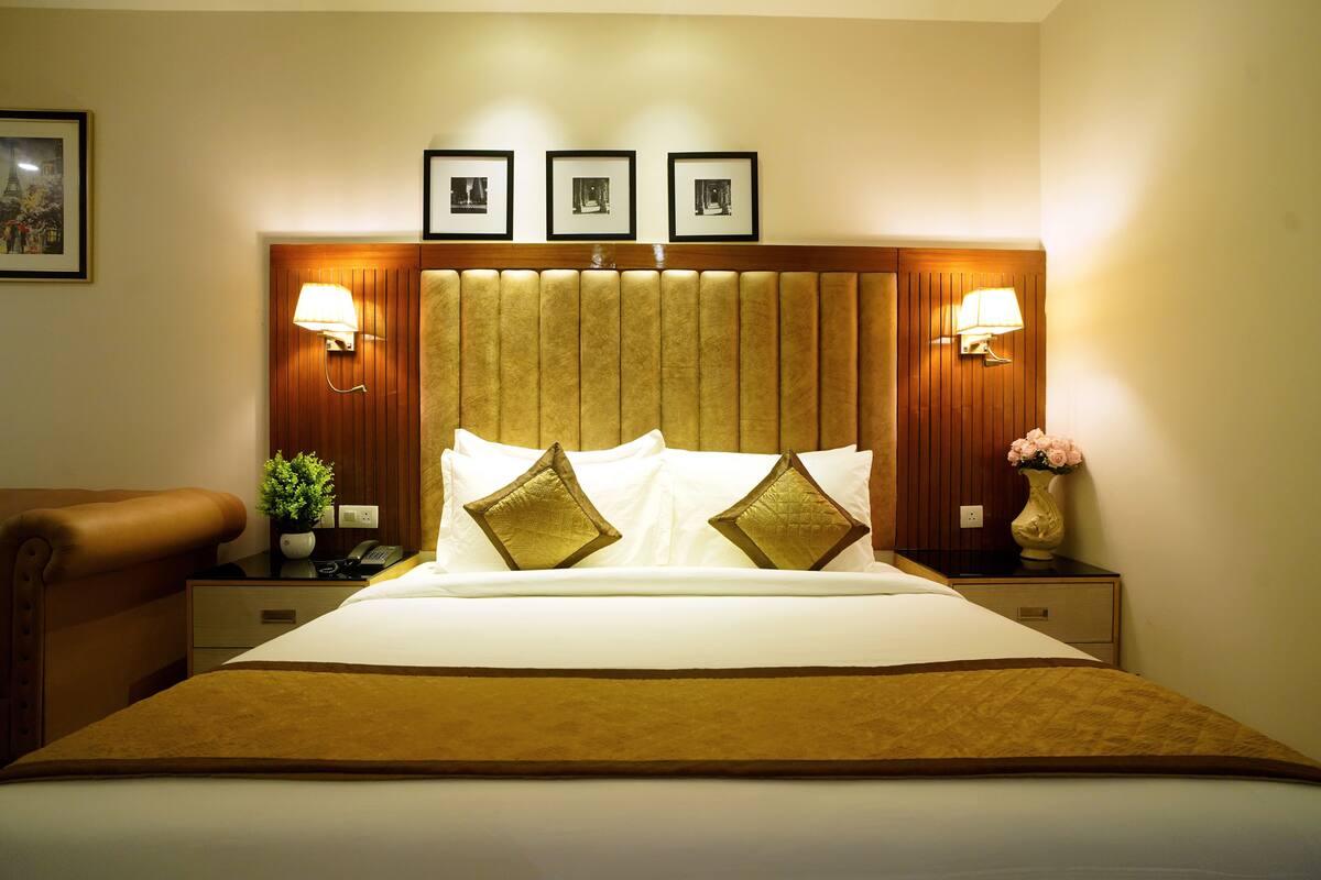 Une chambre d’hôtel avec un grand lit, deux lampes de chevet, une tête de lit en bois et des tableaux encadrés accrochés au mur.