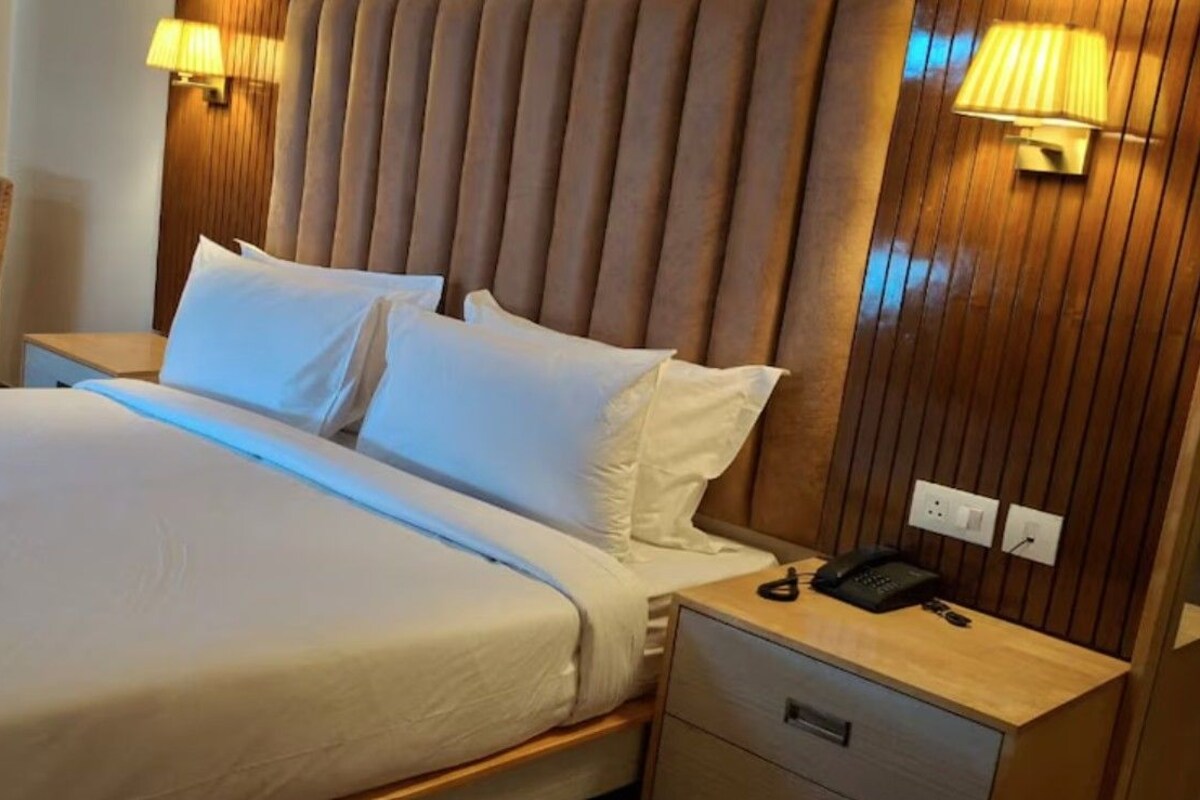 A hotel room with a large bed, two bedside lamps, a wooden headboard, a nightstand with a phone, and a chair.
