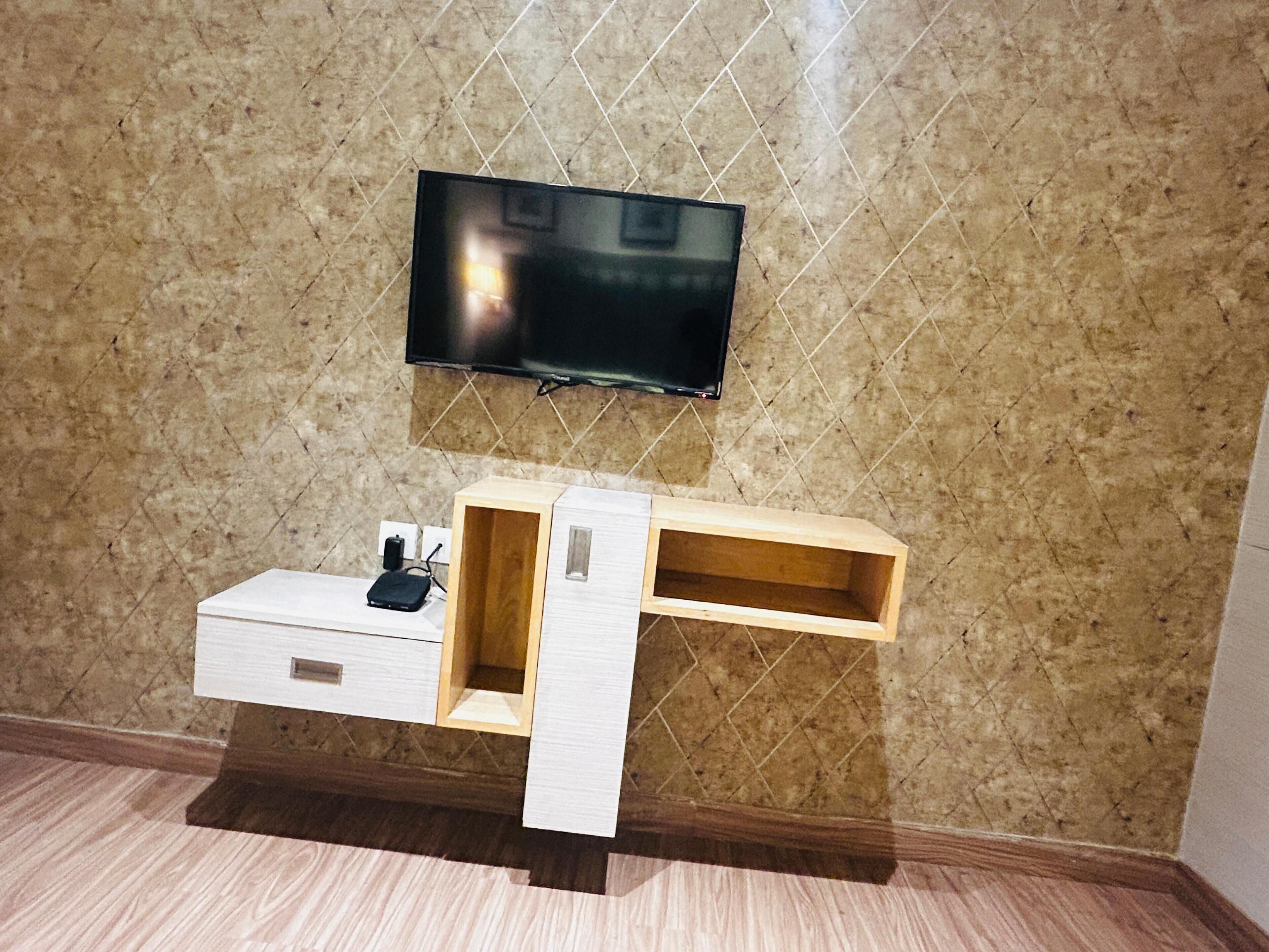 A modern room with a flat-screen TV mounted on a textured wall, a wooden console table with drawers, and a small shelf.
