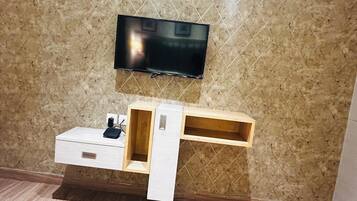 A modern room with a flat-screen TV mounted on a textured wall, a wooden console table with drawers, and a small shelf.